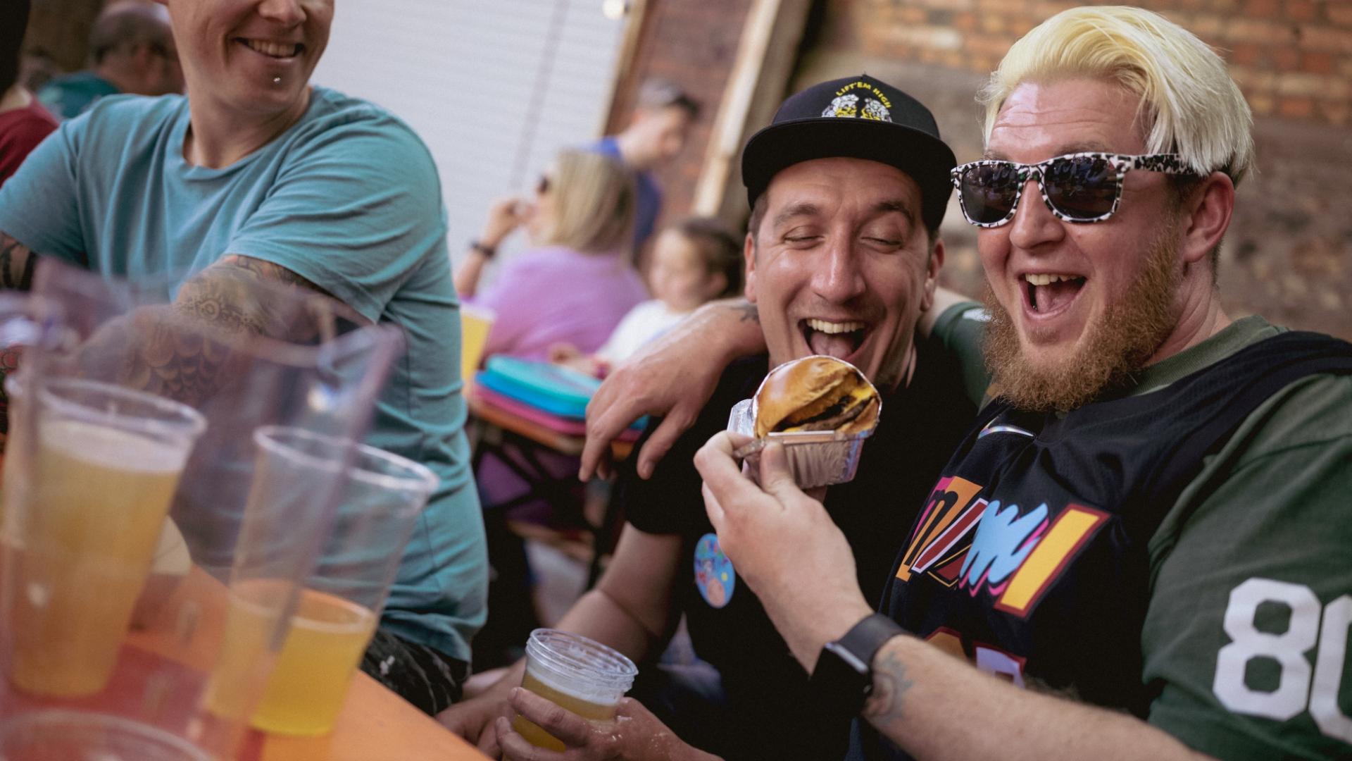 2 male friends smiling holding a burger